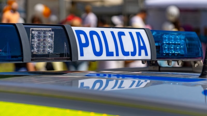 Close-up of a Polish police car light bar with the word "Policja," with blurred figures of people in the background during a public event