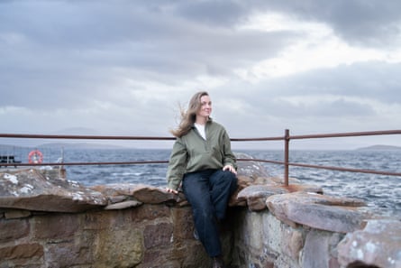 A young woman perched on a rocky wall by the sea