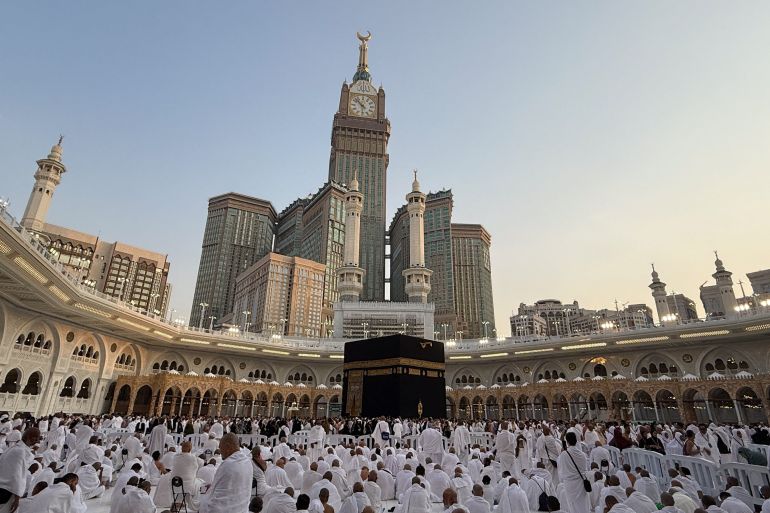 Crowds of pilgrims in white robes move around a large stone structure in a mosque courtyard.