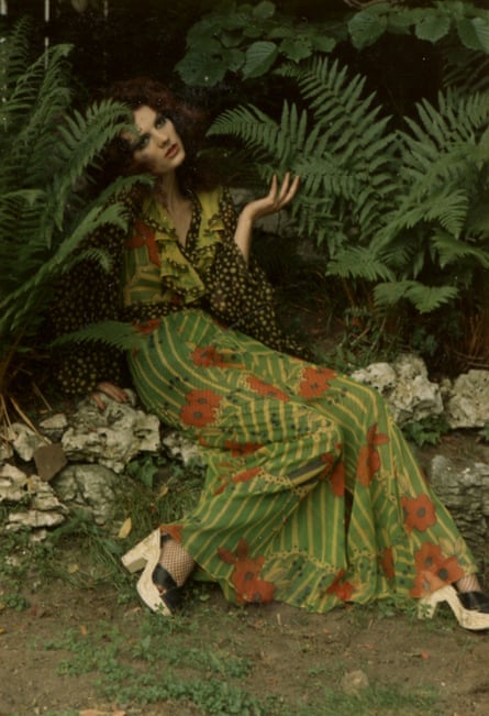 Actor Gala Mitchell reclines in a hedge wearing a long green and red dress
