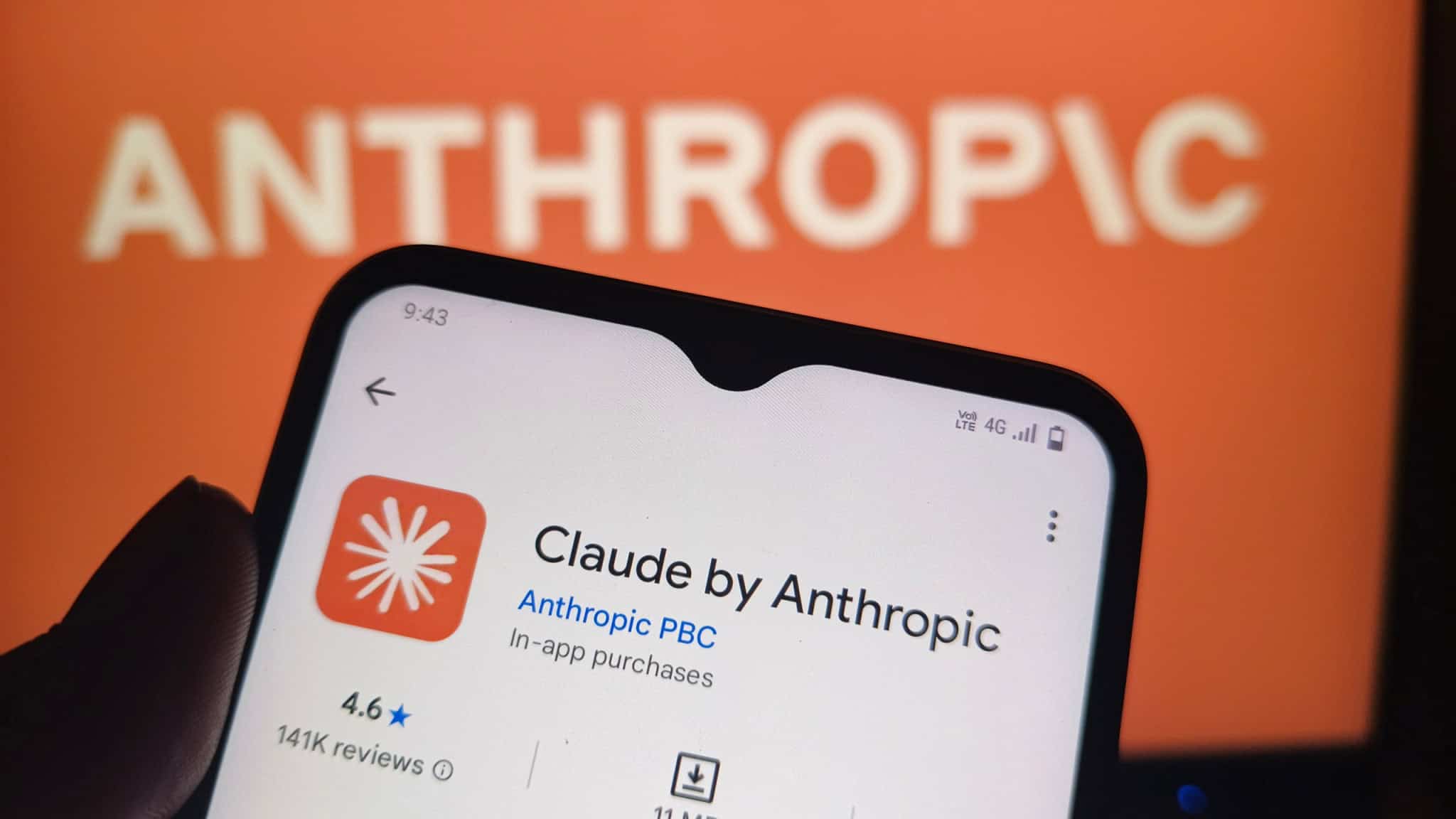 Ao fundo, meio desfocado, logo da Anthropic; à frente, smartphone mostrando a página de download do Claude